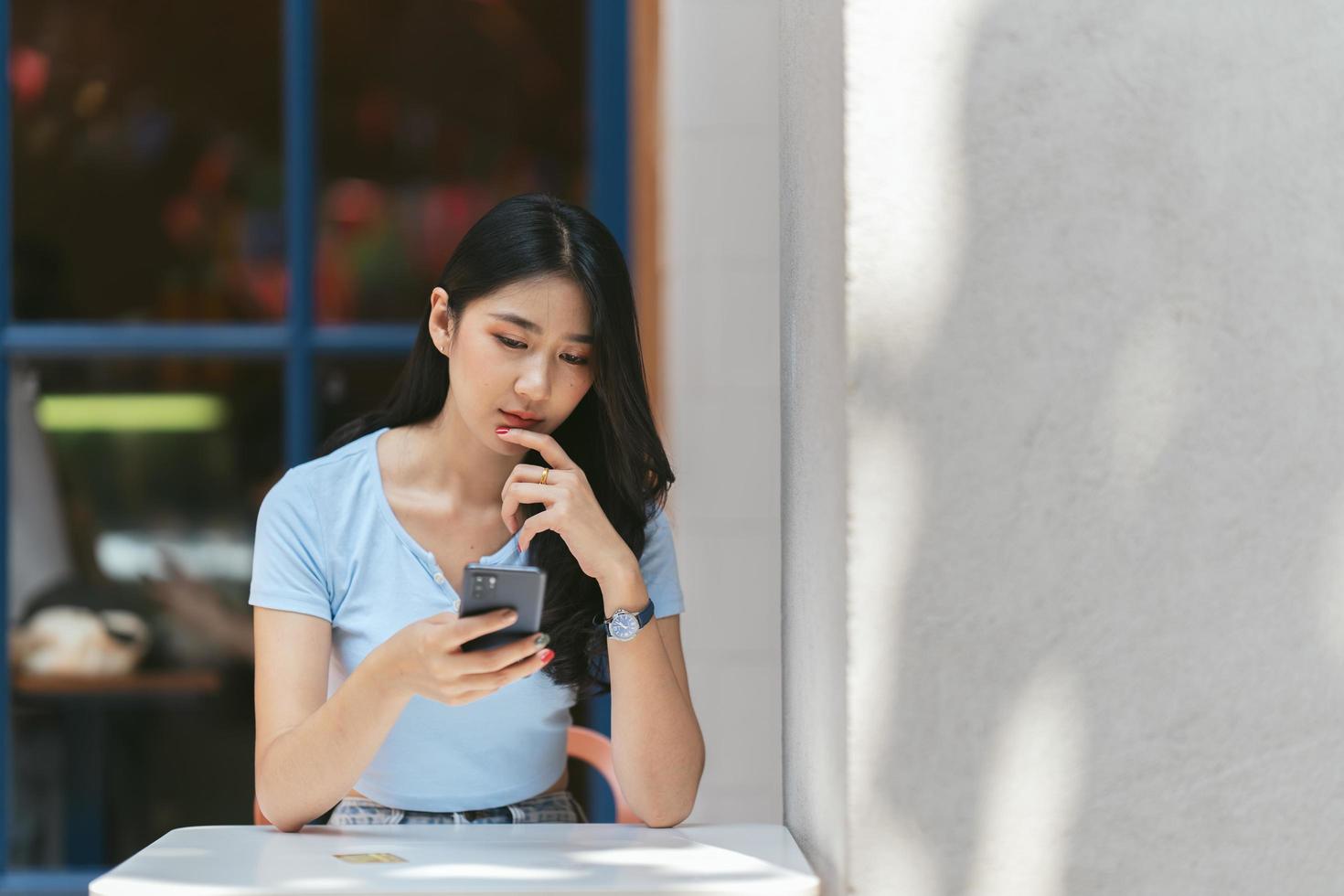 jonge aziatische vrouw die telefoon gebruikt bij een koffiewinkel gelukkig en glimlach. foto