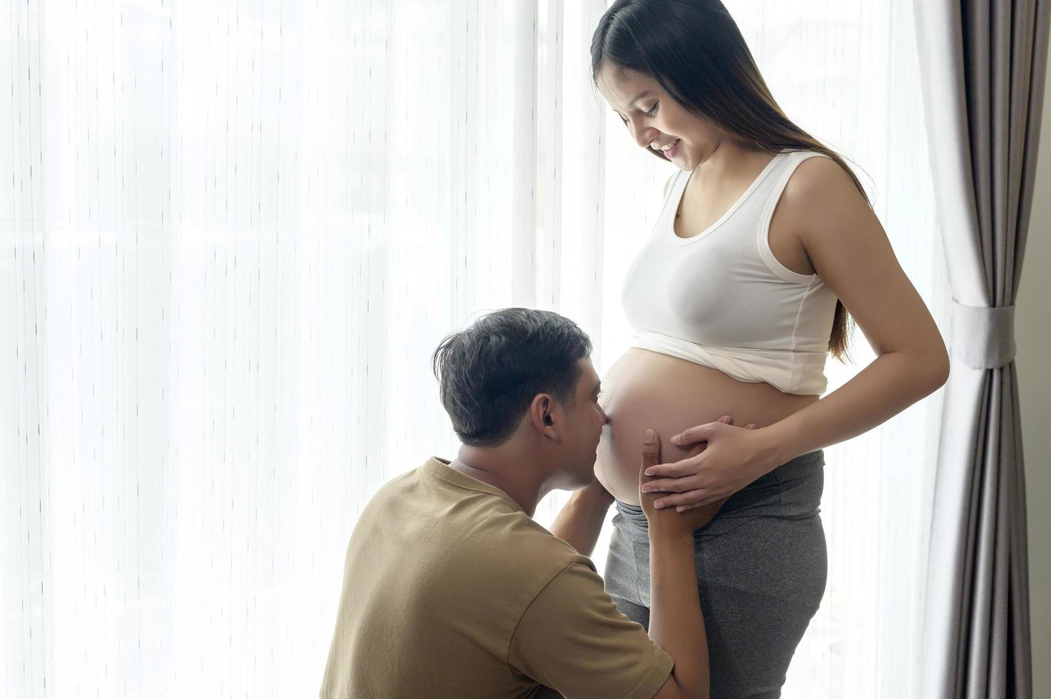 jonge zwangere vrouw met echtgenoot die thuis een baby omhelst en verwacht foto