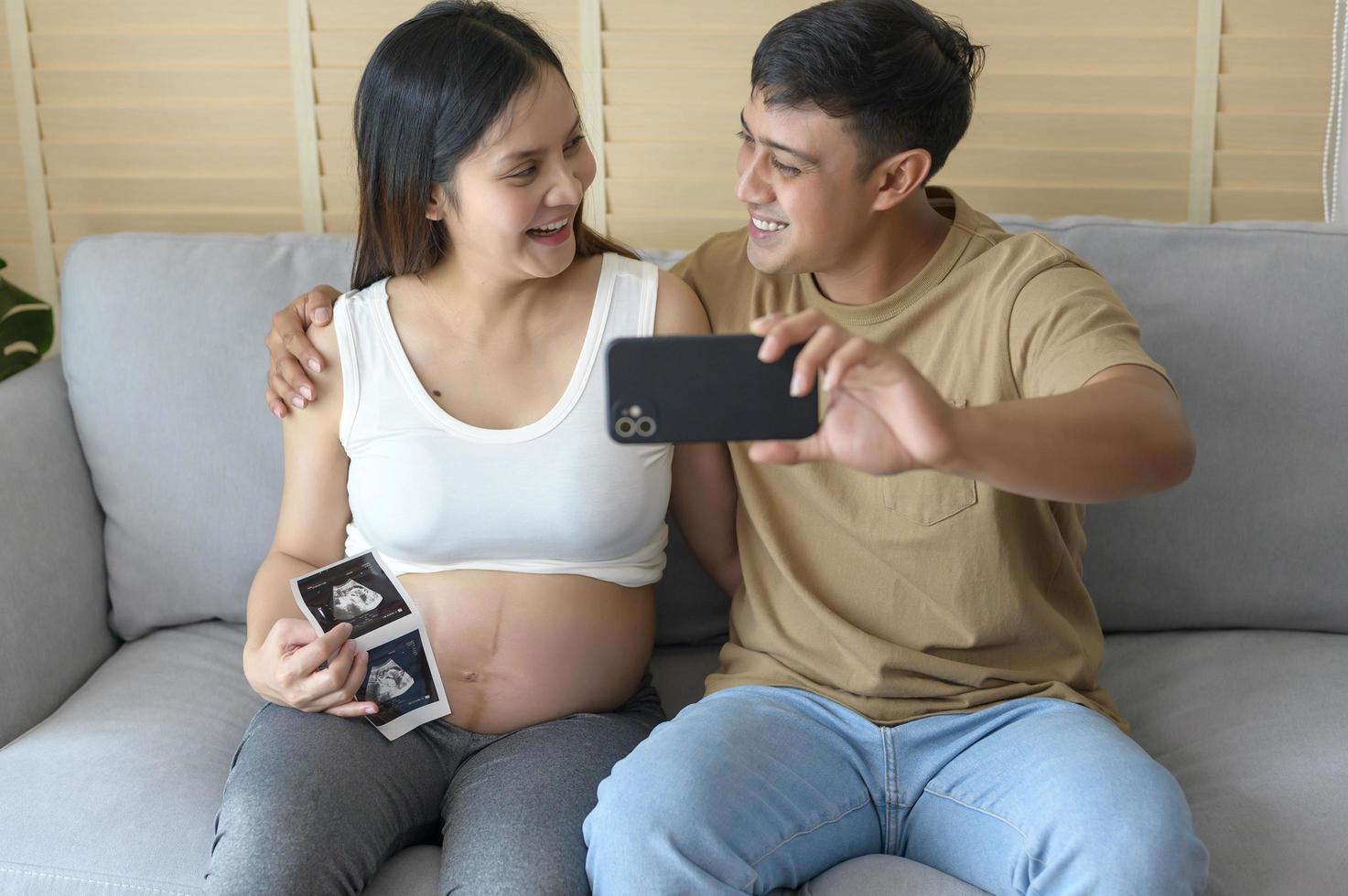 jonge zwangere vrouw met echtgenoot omarmen en videogesprek met familie en vrienden via smartphone op sociale media, familie- en zwangerschapszorgconcept foto