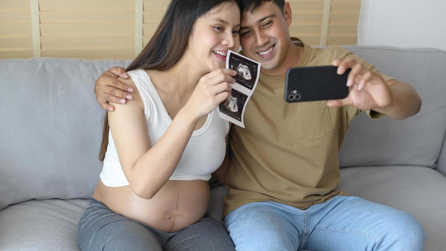 jonge zwangere vrouw met echtgenoot omarmen en videogesprek met familie en vrienden via smartphone op sociale media, familie- en zwangerschapszorgconcept foto