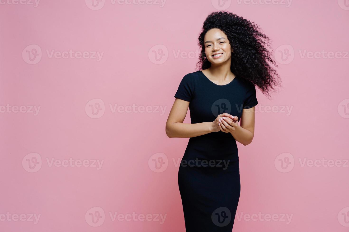 foto van vrolijke vrolijke donkere gekrulde vrouw kleedt zich voor een casual evenement, glimlacht positief, geniet van een aangenaam gesprek met man, houdt de handen bij elkaar, staat binnen, vrije ruimte opzij voor uw tekst