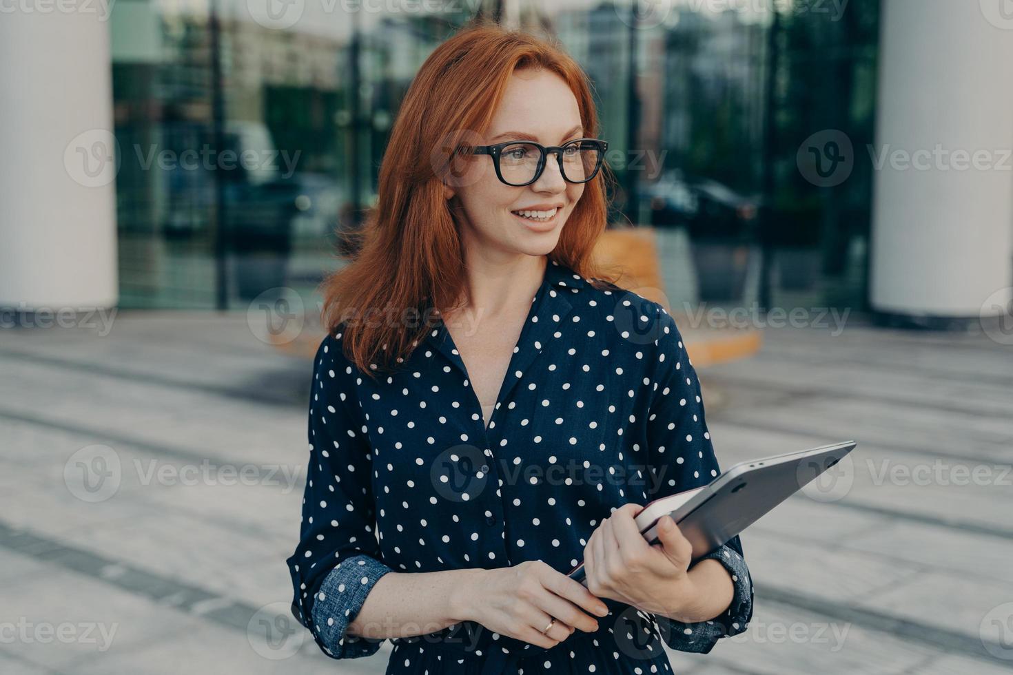 vrouwelijk model draagt laptop en organisator poseert buiten wacht op iemand in de buurt van kantoorgebouw foto