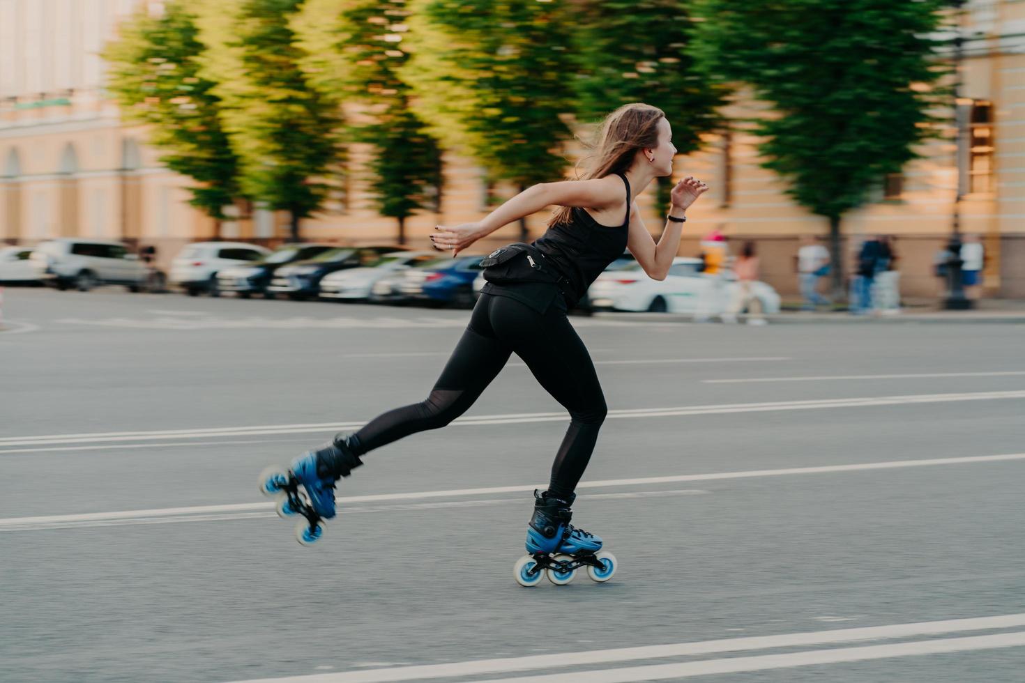 professionele vrouwelijke roller demonstreert haar capaciteiten van skaten rijdt heel snel op de weg langs de stad geniet van een zonnige dag gekleed in zwarte actieve kleding. actieve levensstijl hobby en fitness activiteit foto