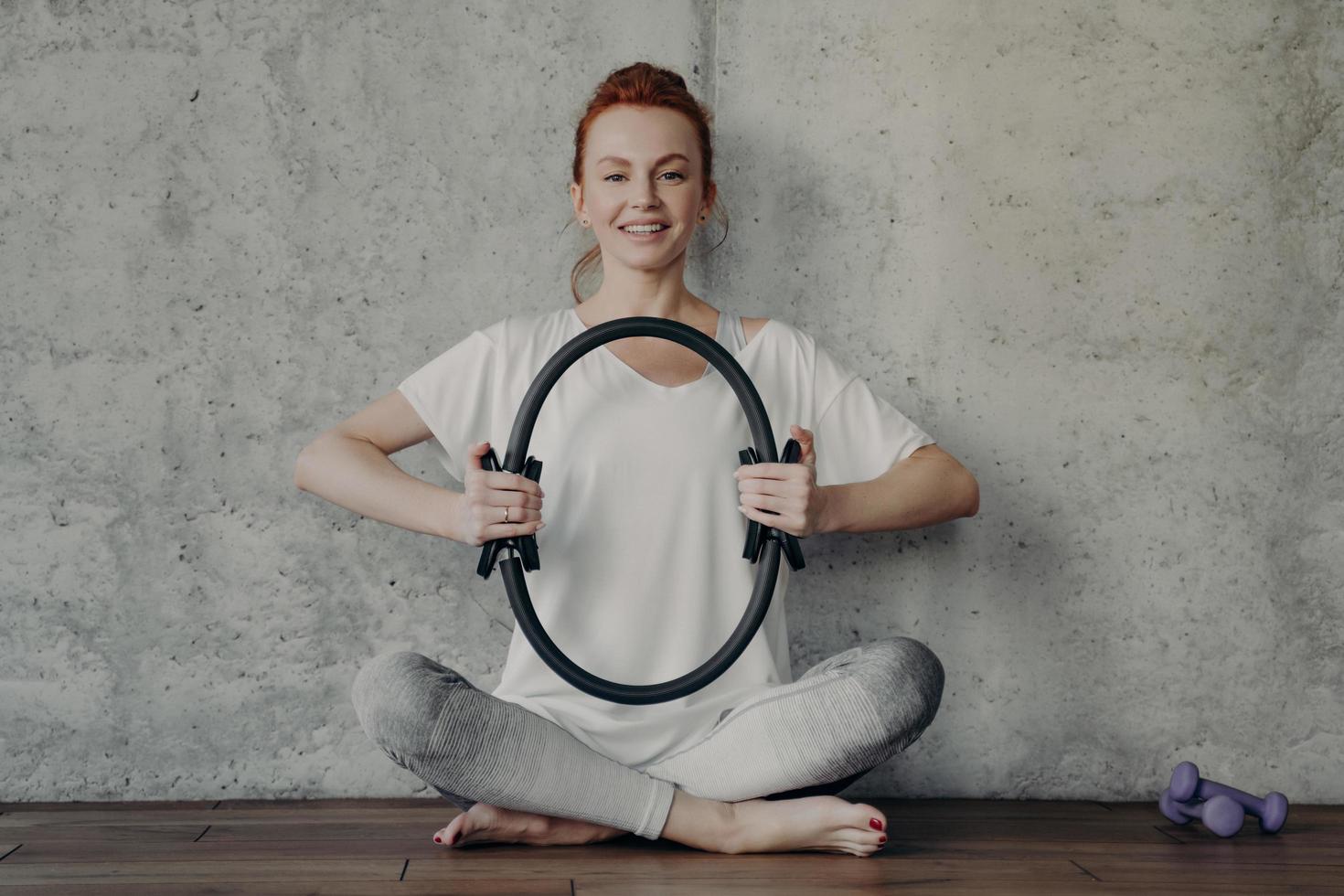 vrolijke fitness vrouw in actieve slijtage zittend in lotushouding en oefenen met pilates ring foto