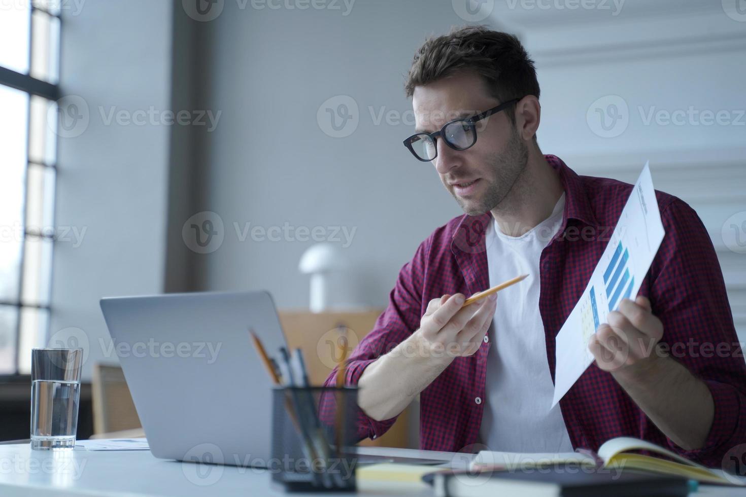 jonge europese man kantoormedewerker in glazen met statistiekenrapport tijdens online vergadering foto