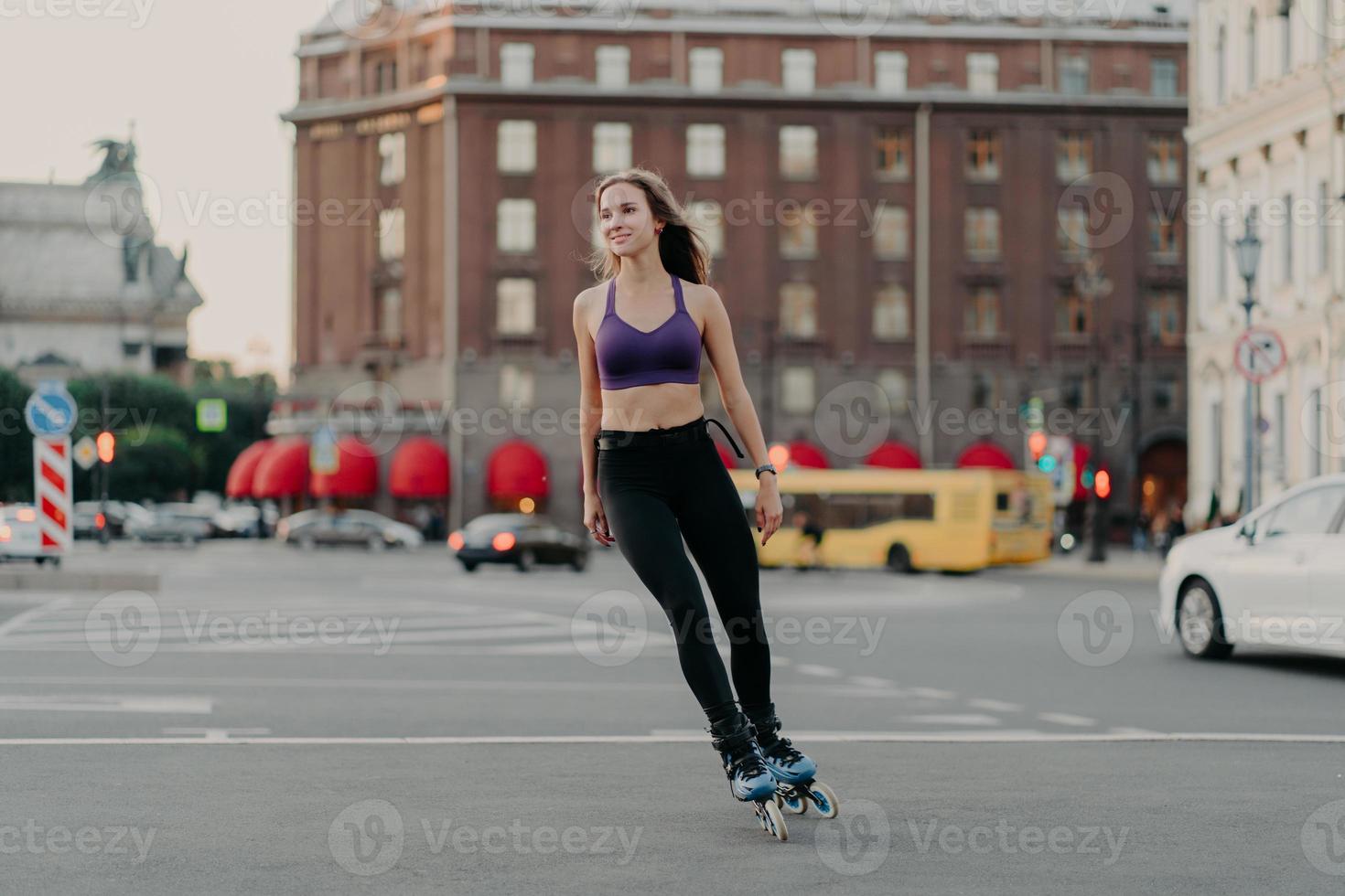 volledige lengte shot van sportieve slanke vrouw in actieve slijtage rijdt op bladen geniet van outdoor fitness-activiteit tijdens warme zomerdag poses op stedelijke plaats op asfalt. skate- en vrijetijdsconcept foto