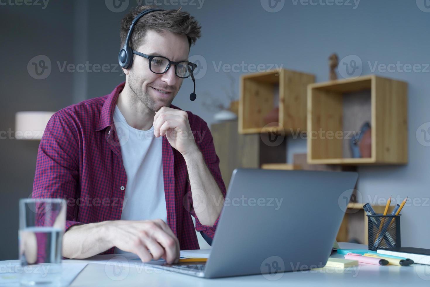 lachende Duitse man die thuis zit in een draadloze headset en deelneemt aan onlinevergaderingen foto