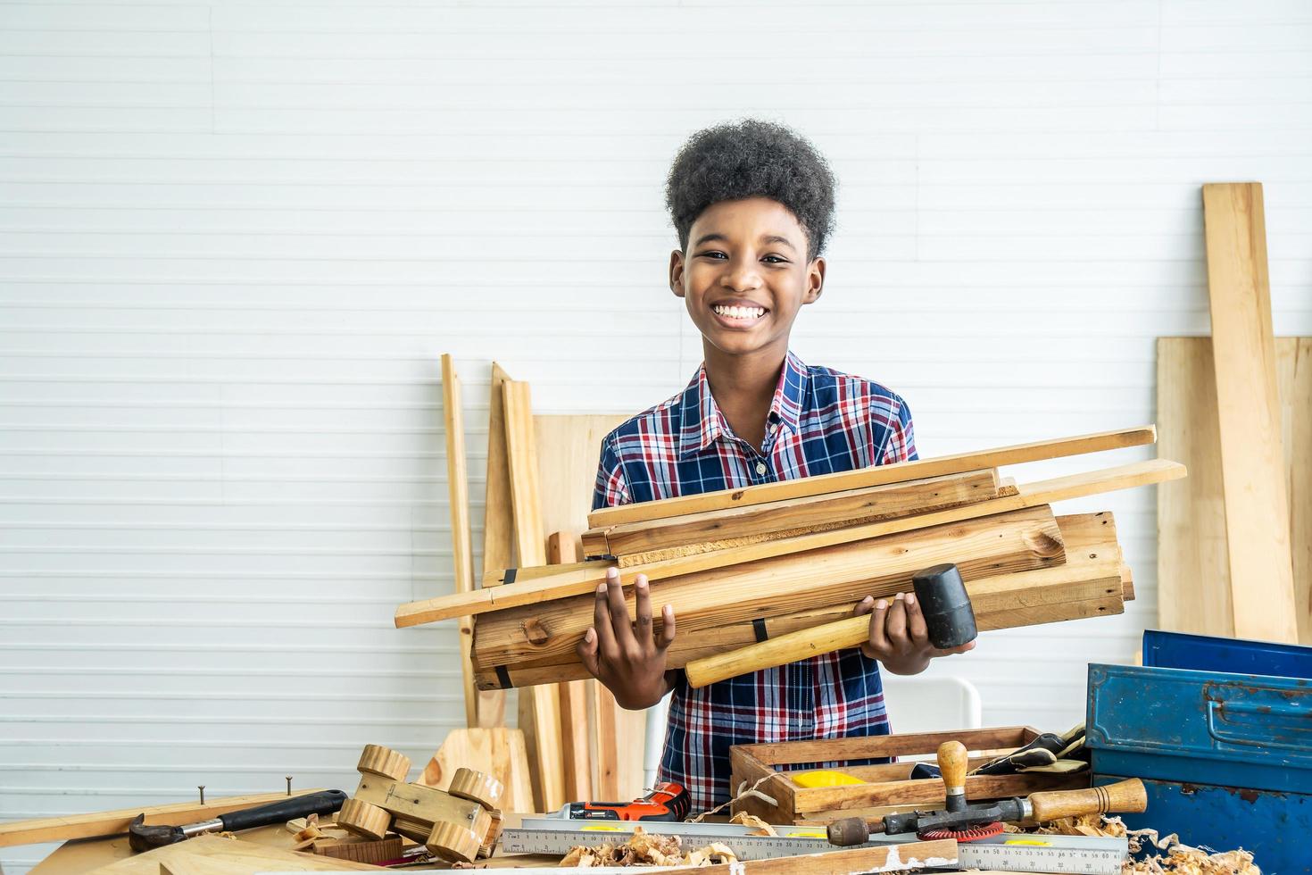 glimlachende Afro-Amerikaanse jongen timmerman staande houdt verschillende stukken hout vast om vader te helpen zich voor te bereiden op het maken van houtbewerkingsambachten foto