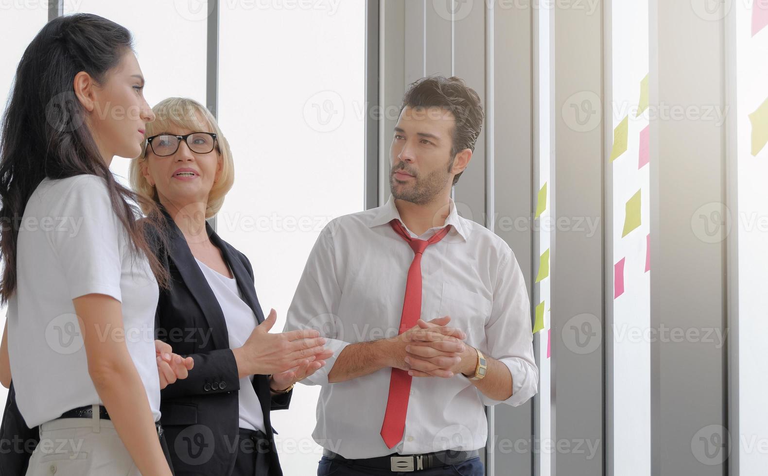 diversiteit zakenmensen staan te discussiëren bij het raamkantoor. senior bril vrouwelijke manager vriendelijk praten met personeel tijdens strategie briefing, lichteffect. foto