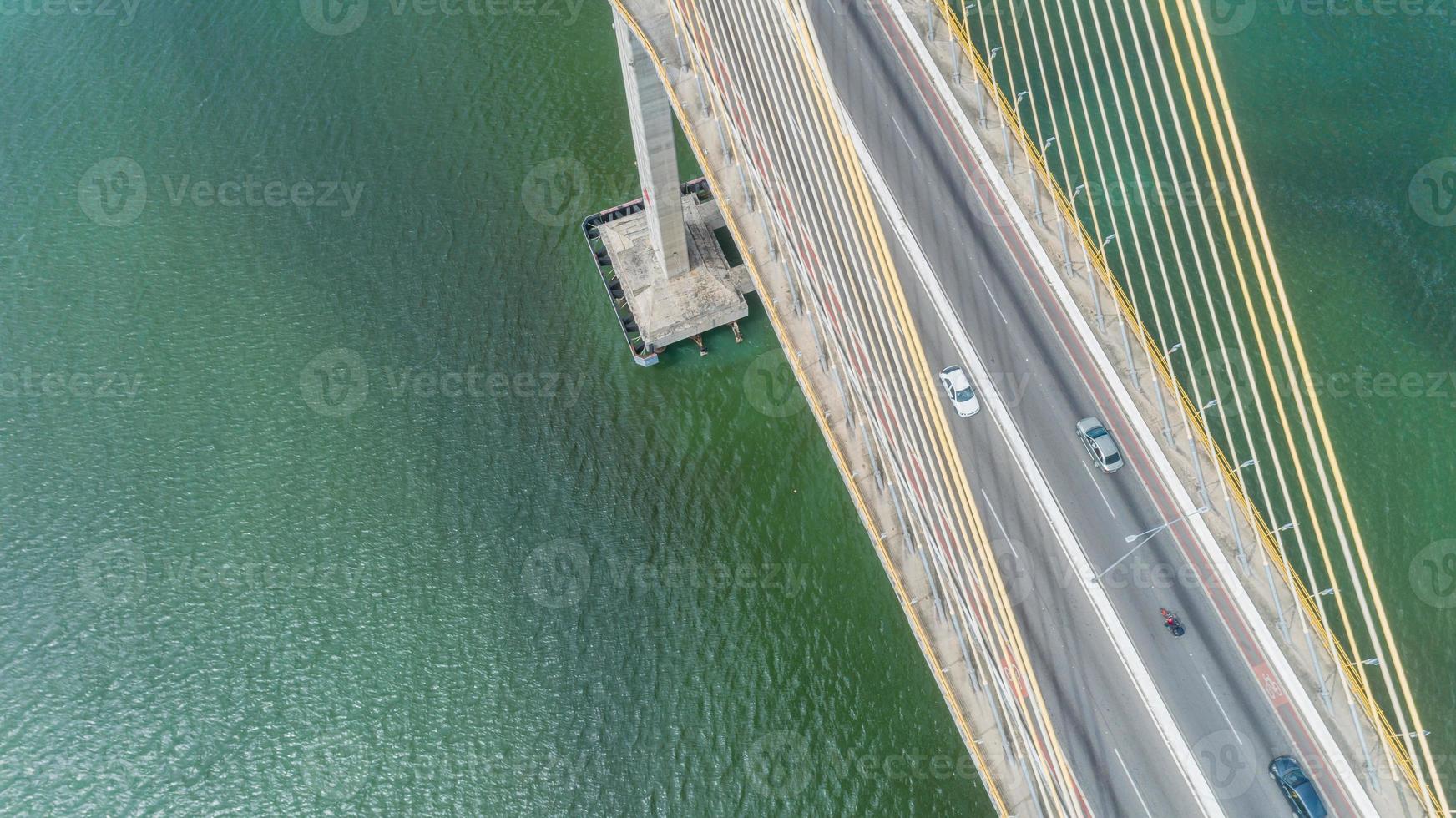 luchtfoto van auto rijden op een brug met natuurlijke bosbomen, zand, tropisch strand en golven die de kust in rollen. foto