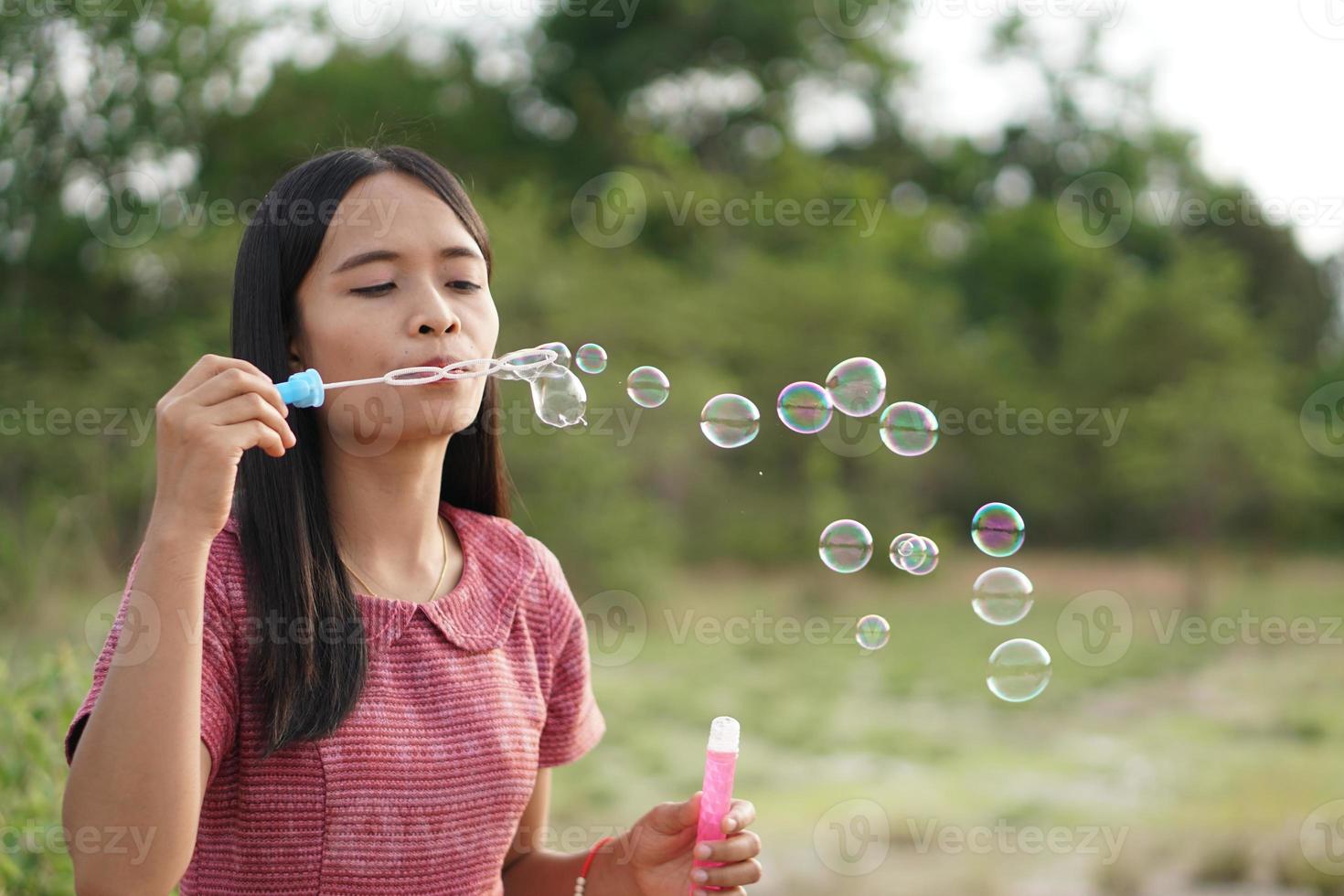 Aziatische vrouw die zeepbellen blaast op elke groene grasachtergrond foto