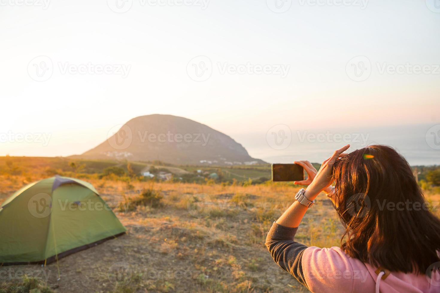 vrouw maakt foto's van de zonsopgang in de bergen op haar telefoon. selfie in de rijzende zon. panoramisch zicht op zee en ayu-dag. kamperen, buitenactiviteiten, sport bergwandelen, gezinsreizen. Krim. foto