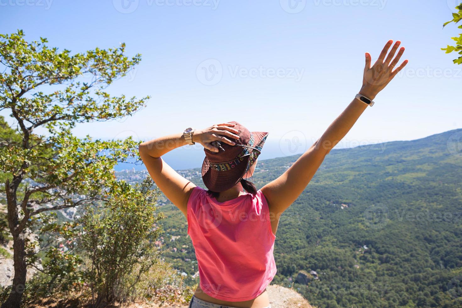 vrouw in een hoed kijkt naar het panoramische uitzicht vanaf de berg naar de zee en het bos. toerist, trekking, reizen. actief ecotoerisme, gezonde levensstijl, avontuur foto
