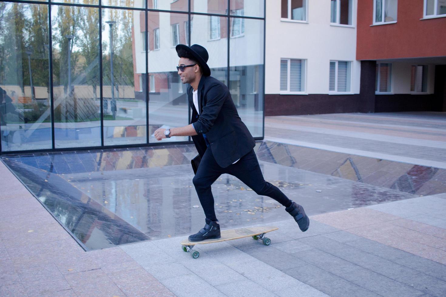 concept van jonge, snelle en mobiele manager. grappige buisinessman op skateboard in zwart pak. foto