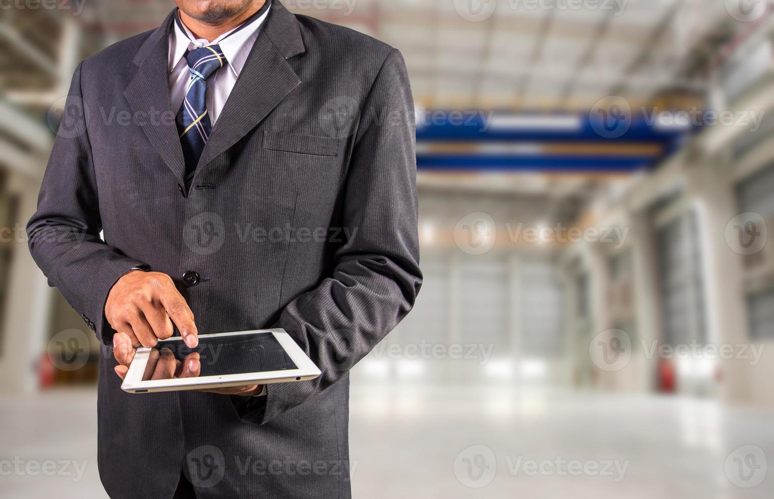 zakenman houdt tablet vast met fabrieksachtergrond foto