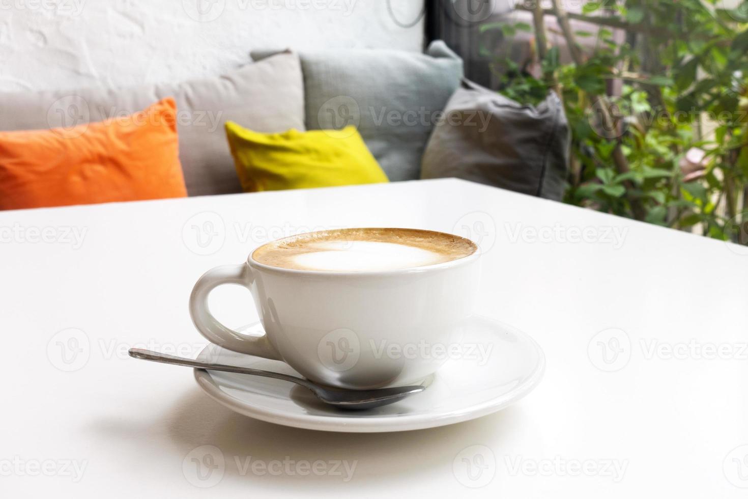 warme koffie op de witte tafel in het café bij de bank en het glazen raam. foto