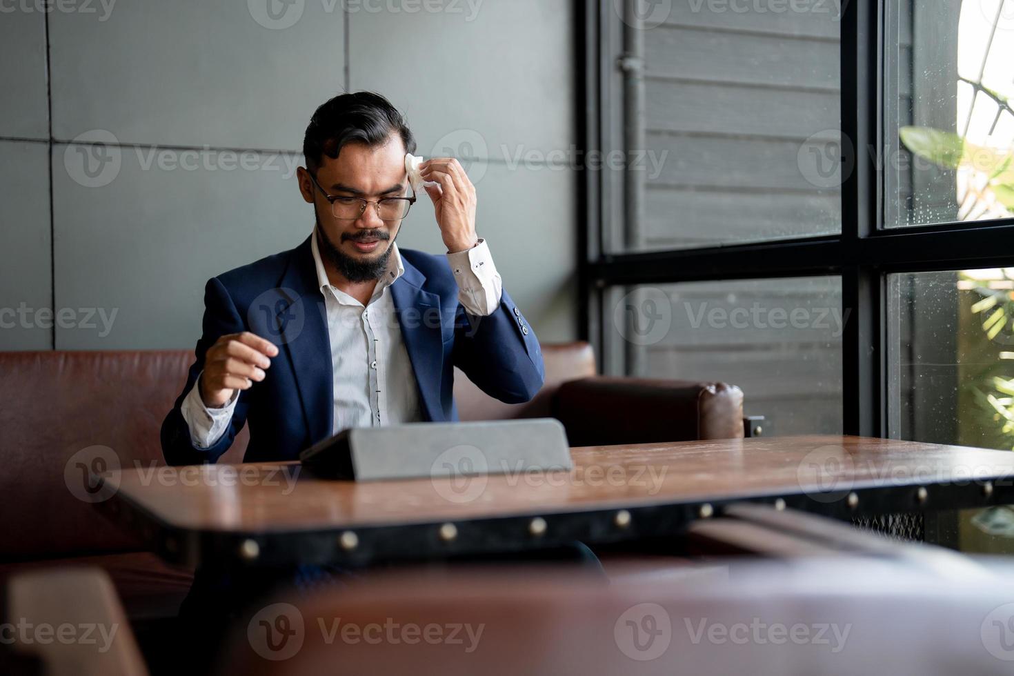 zakenman kijkt naar zijn laptop en gebruikt papieren zakdoekje om zweet af te vegen. foto