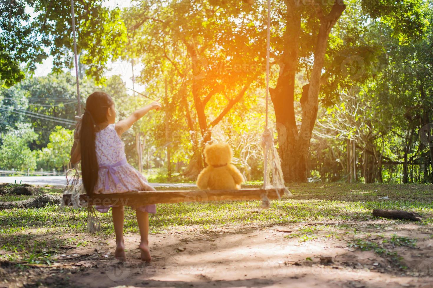 een klein meisje en een teddybeer zittend op een schommel. foto