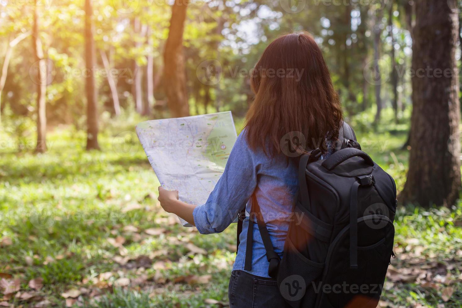 vrouwelijke wandelaar met rugzak controleert kaart om routebeschrijving in wildernisgebied te vinden foto