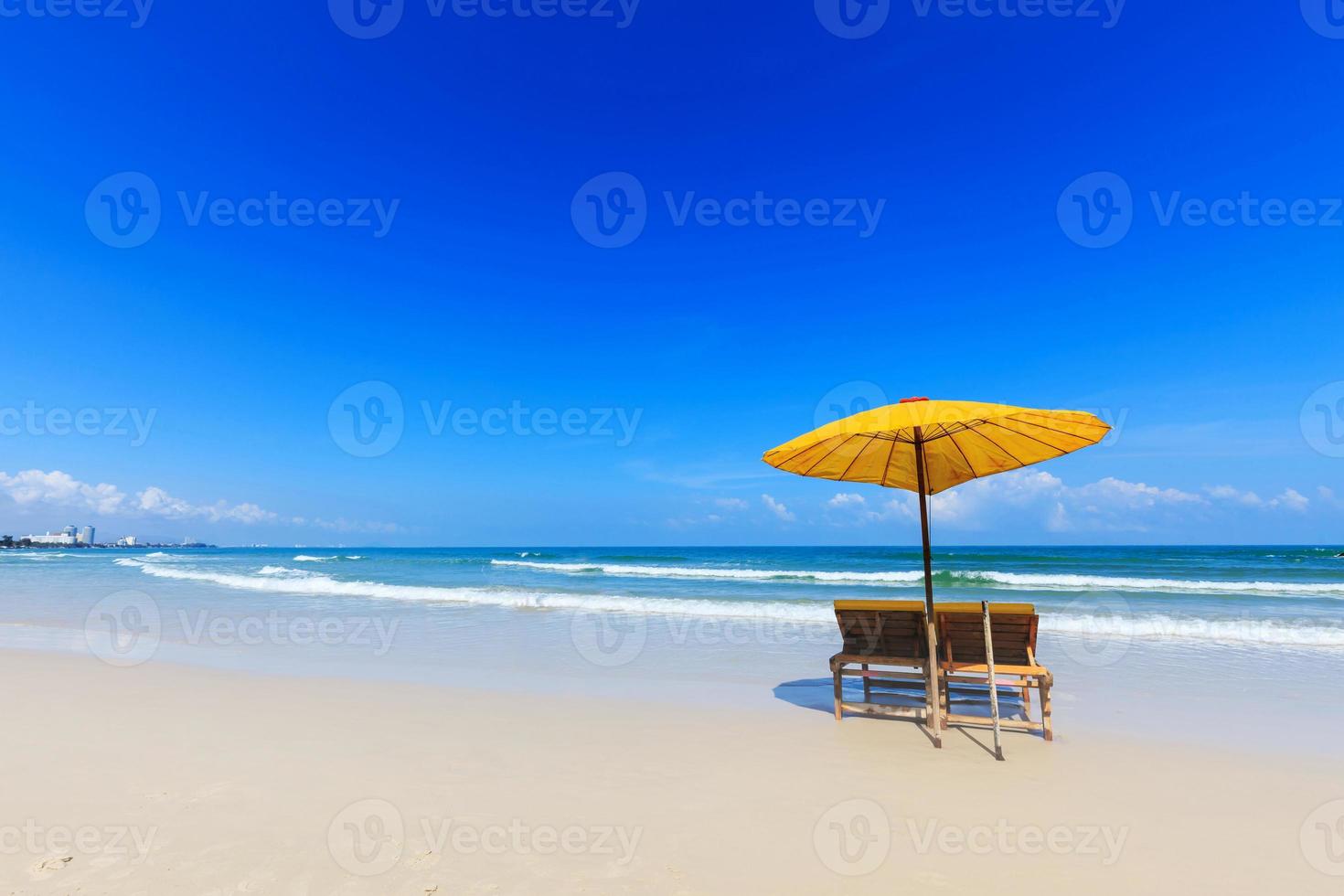 gele parasol en houten stoelen op het strand foto