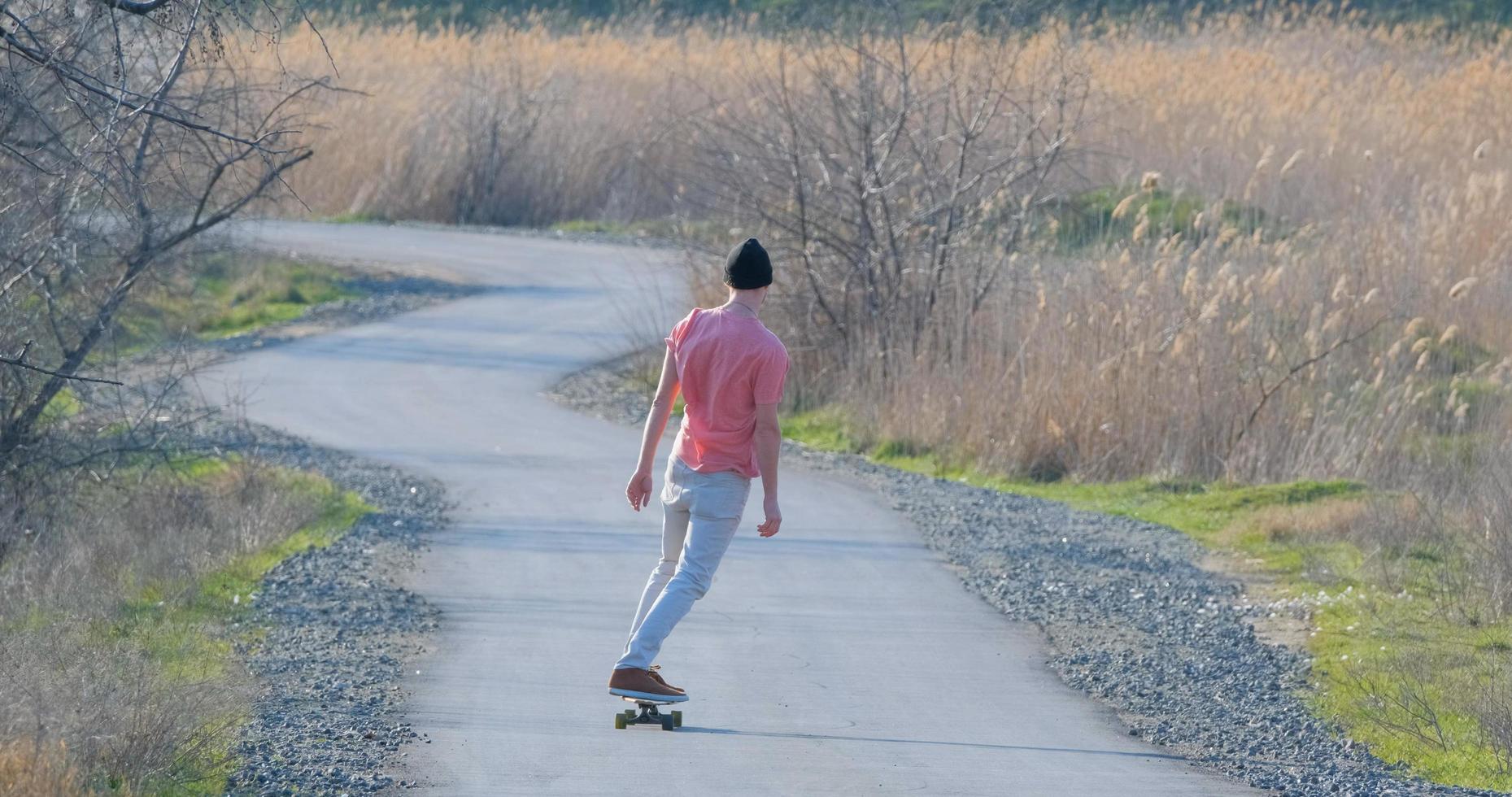 jonge mannelijke rit op longboard skateboard op de landweg in zonnige dag foto