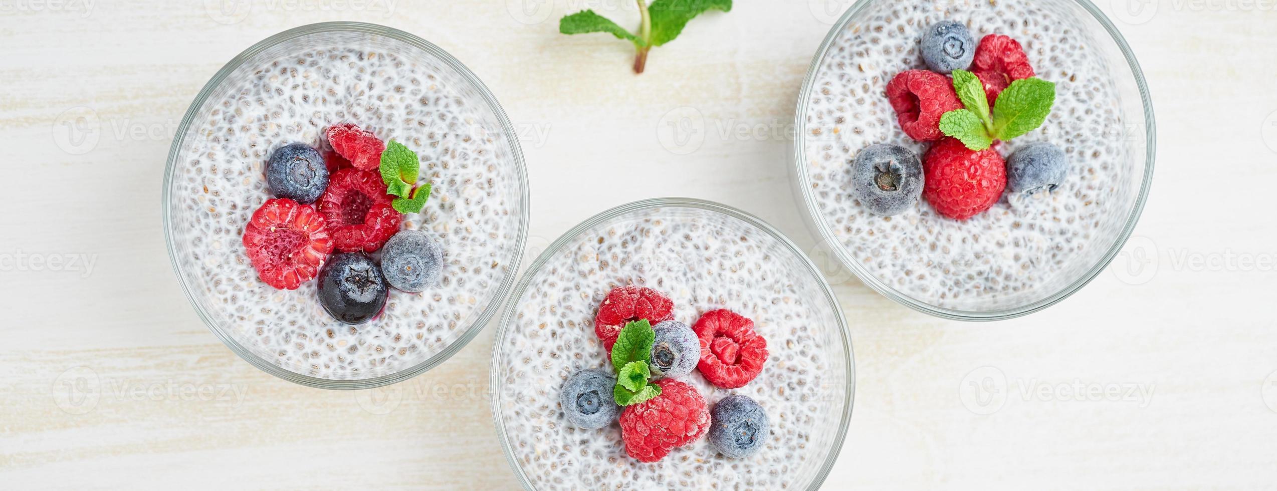 lange banner met chia pudding met verse bessen frambozen, bosbessen. drie glas, bovenaanzicht. foto