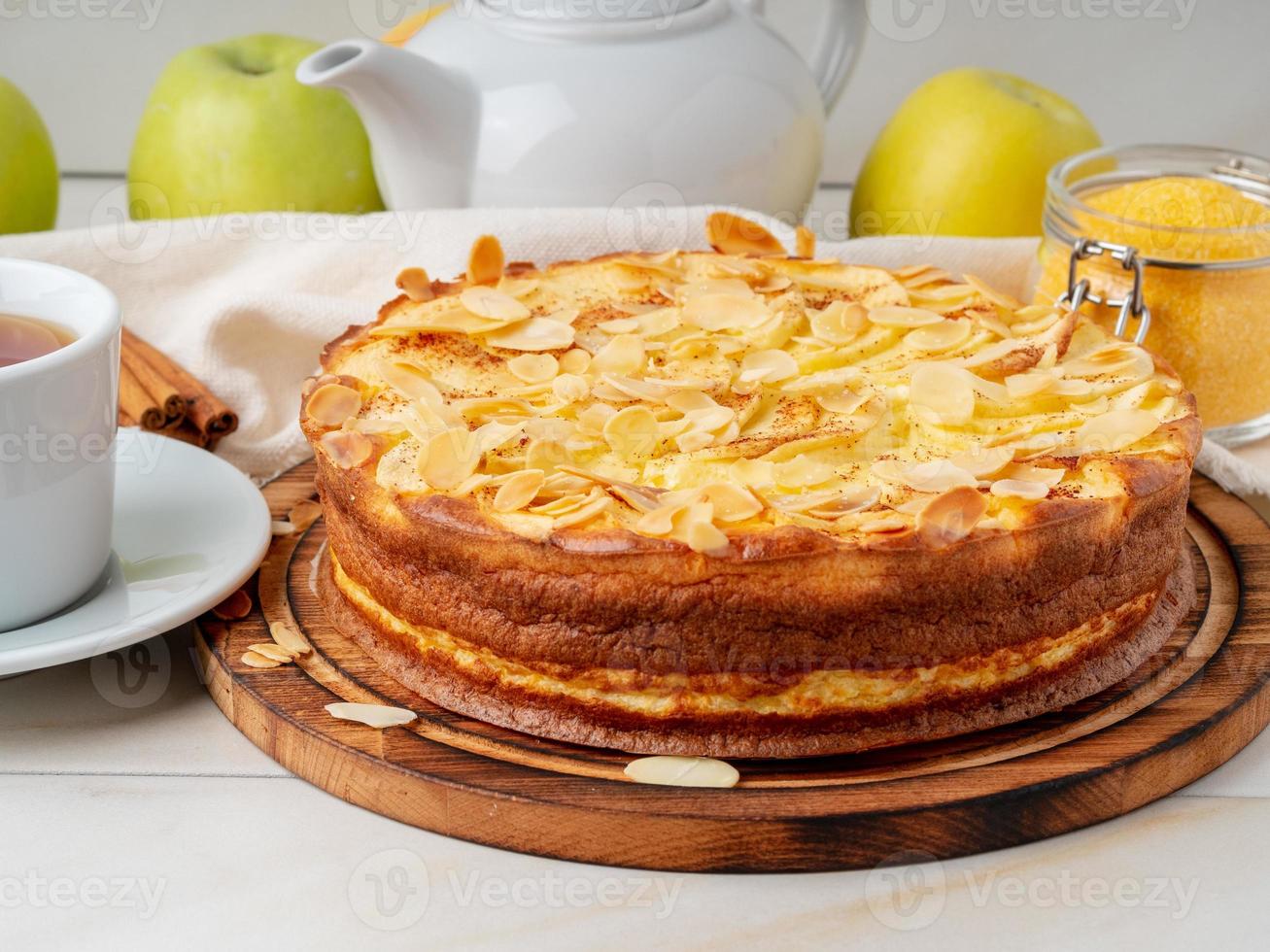 cheesecake, appeltaart, wrongeldessert met polenta, appels, amandelvlokken en kaneel op witte marmeren keukentafel, zijaanzicht foto