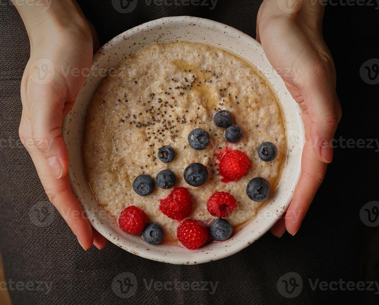 donkere voedselfotografie. plaat met pap in de hand op donkere achtergrond, bovenaanzicht. gezond ontbijt met frambozen en bosbessen, chiazaden, ahornsiroop. foto