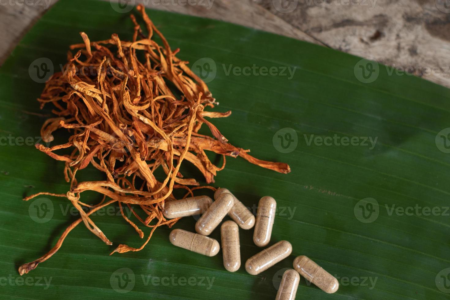 droge cordyceps militaris op een groen bananenblad met houten achtergrond. oranje medische paddenstoel voor een goede gezondheid met capsules. foto