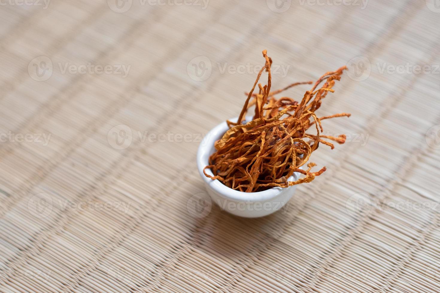 droge mycelium van cordyceps militaris in witte kom met houten achtergrond. oranje medische paddenstoel voor een goede gezondheid. foto