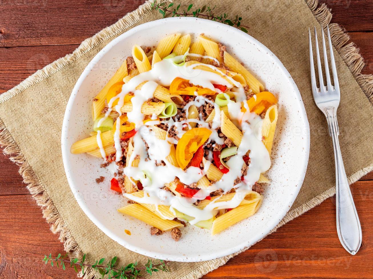 penne pasta met gele tomaten, groenten, gehakt, witte saus op donkere houten ondergrond, bovenaanzicht, close-up foto