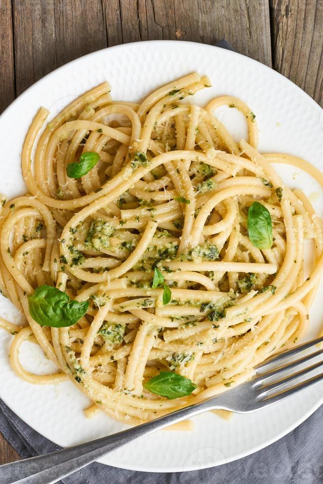 pesto spaghetti pasta met basilicum, knoflook, pijnboompitten, olijfolie. verticaal. rustieke tafel foto