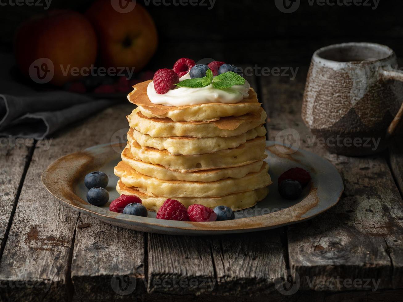 pannenkoek met vanilleroom, bosbessen en frambozen. zijaanzicht. donkere humeurig oude rustieke houten achtergrond. foto