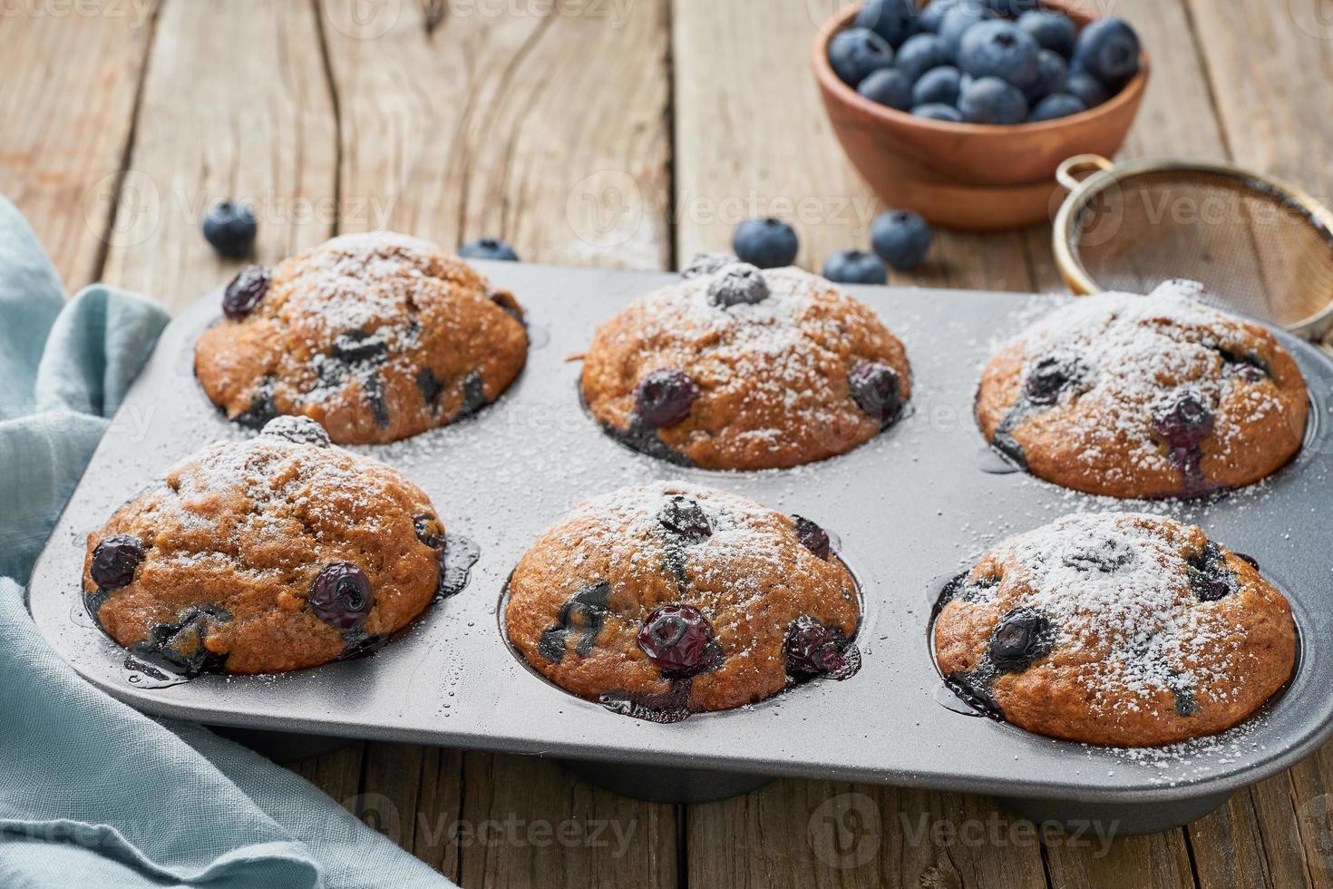 bosbessenmuffin in dienblad, zijaanzicht. cupcakes met bessen in ovenschaal op oud linnen servet, rustieke houten tafel, ontbijt met cake foto