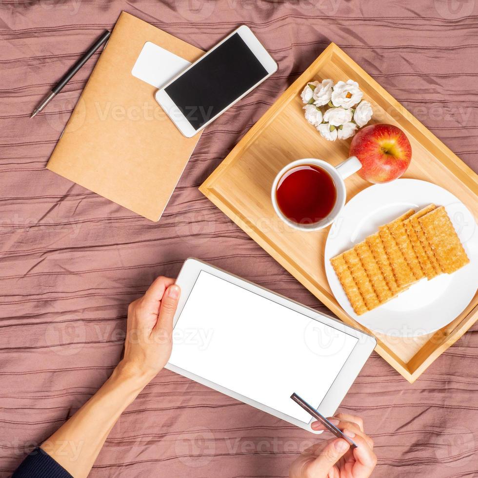 vrouw liggend op bed, thee drinken en kijken naar tablet, betalen voor aankopen, online winkelen foto