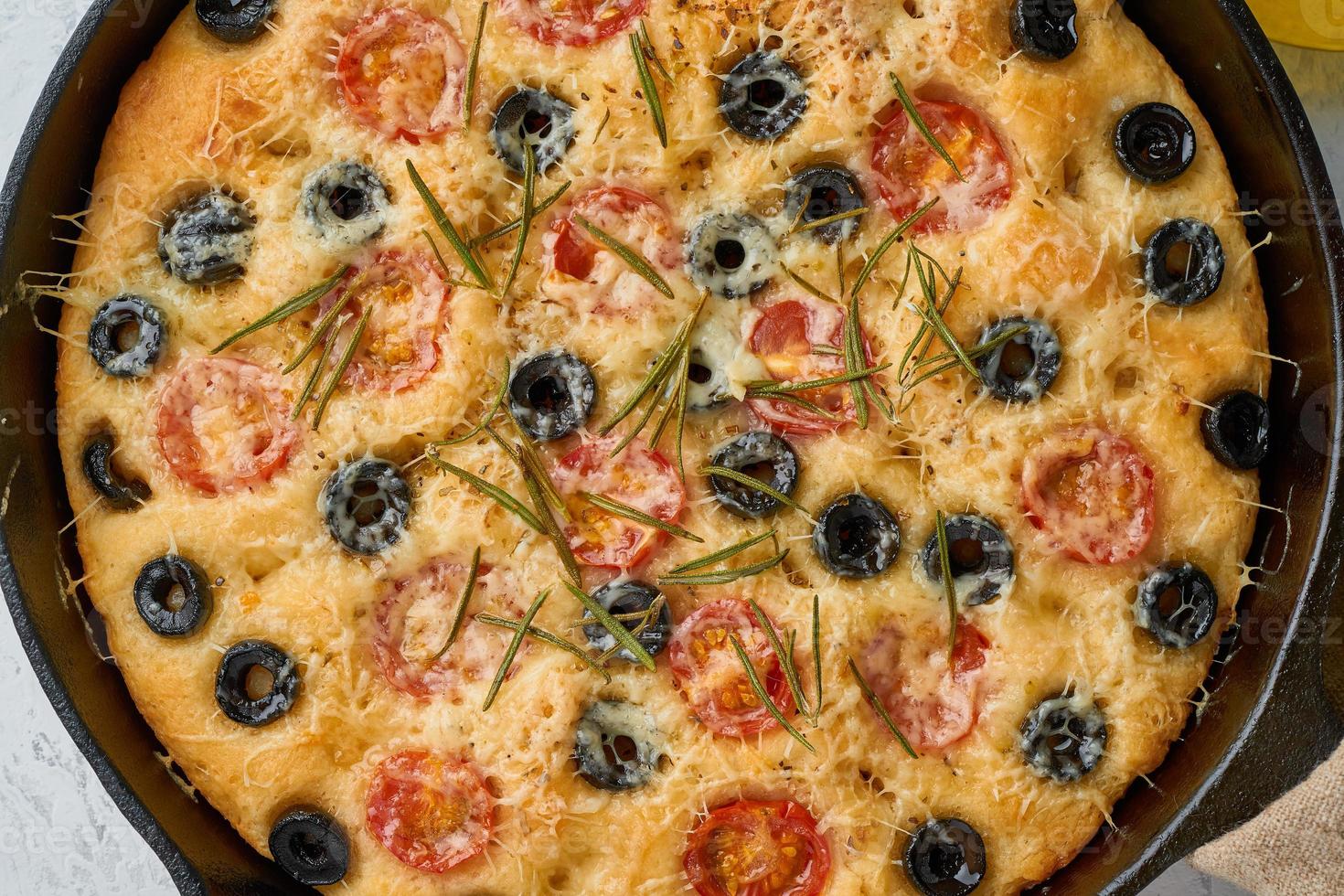 focaccia, pizza in koekenpan, Italiaans plat brood met tomaten, olijven en rozemarijn. houten tafel foto