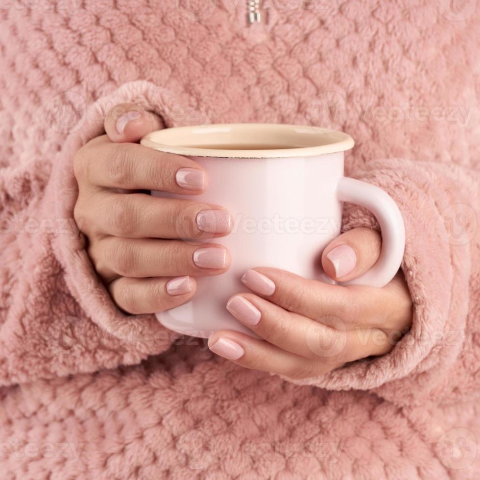 handen met kopje thee of koffie, roze huiskamerjas, mooie roze manicure, huisstijl, herfstochtend, close-up foto