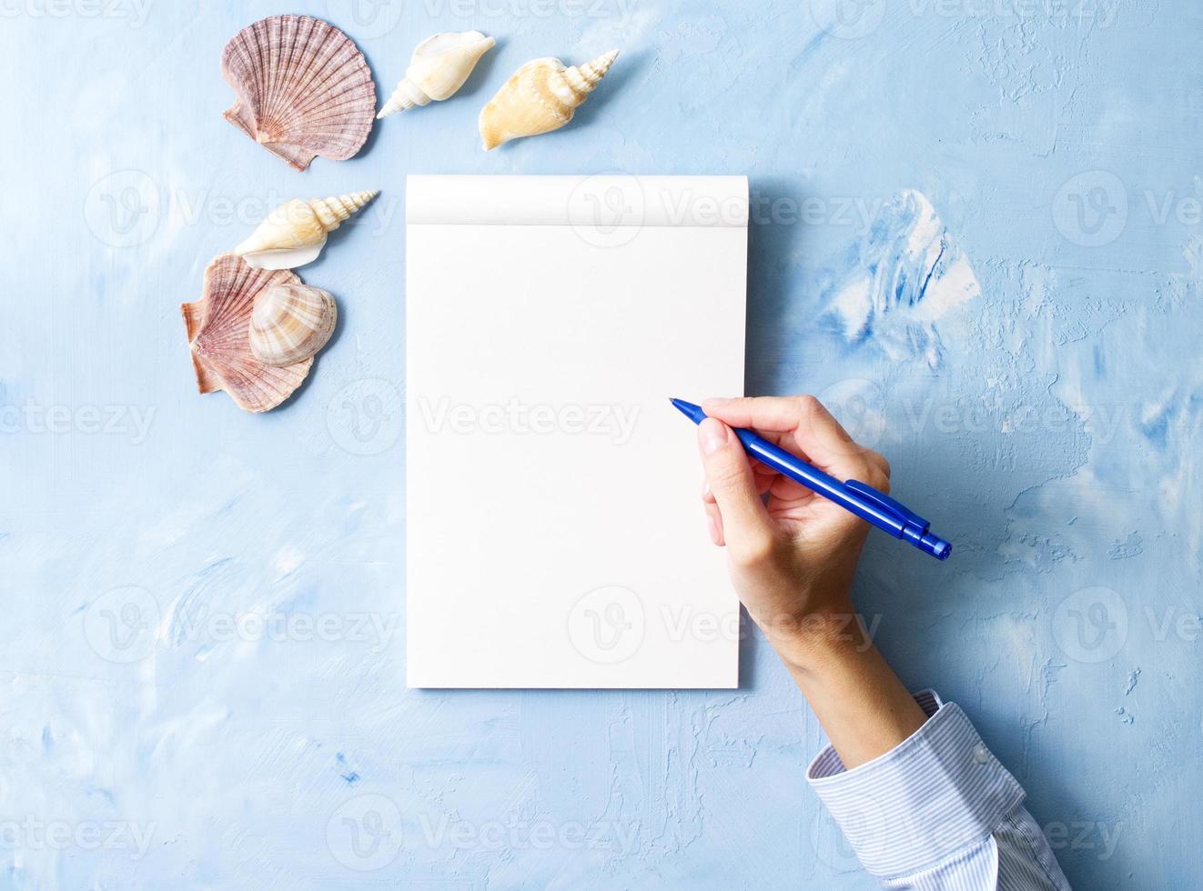 vrouw schrijft in notitieboekje op steenblauwe tafel, bespotten met frame van zeeschelp, bovenaanzicht foto