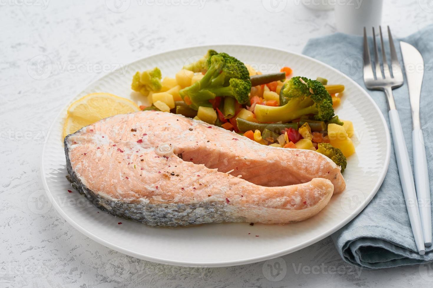 stoom zalm en groenten, gezonde voeding. witte plaat op betonnen tafel, zijaanzicht foto