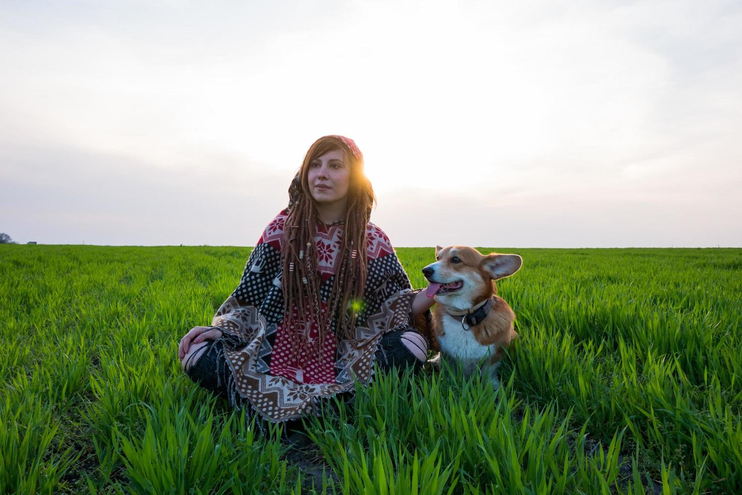 jonge vrouw in poncho met corgi hond ontspannen in de lente velden foto