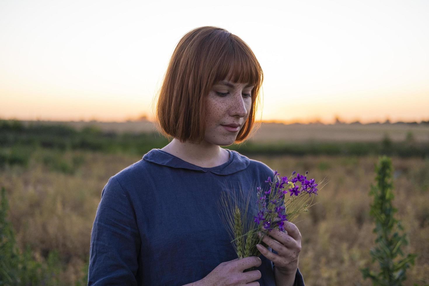 jonge roodharige vrouw met sproeten in vintage handgemaakte jurk lopen in velden met bloemen foto