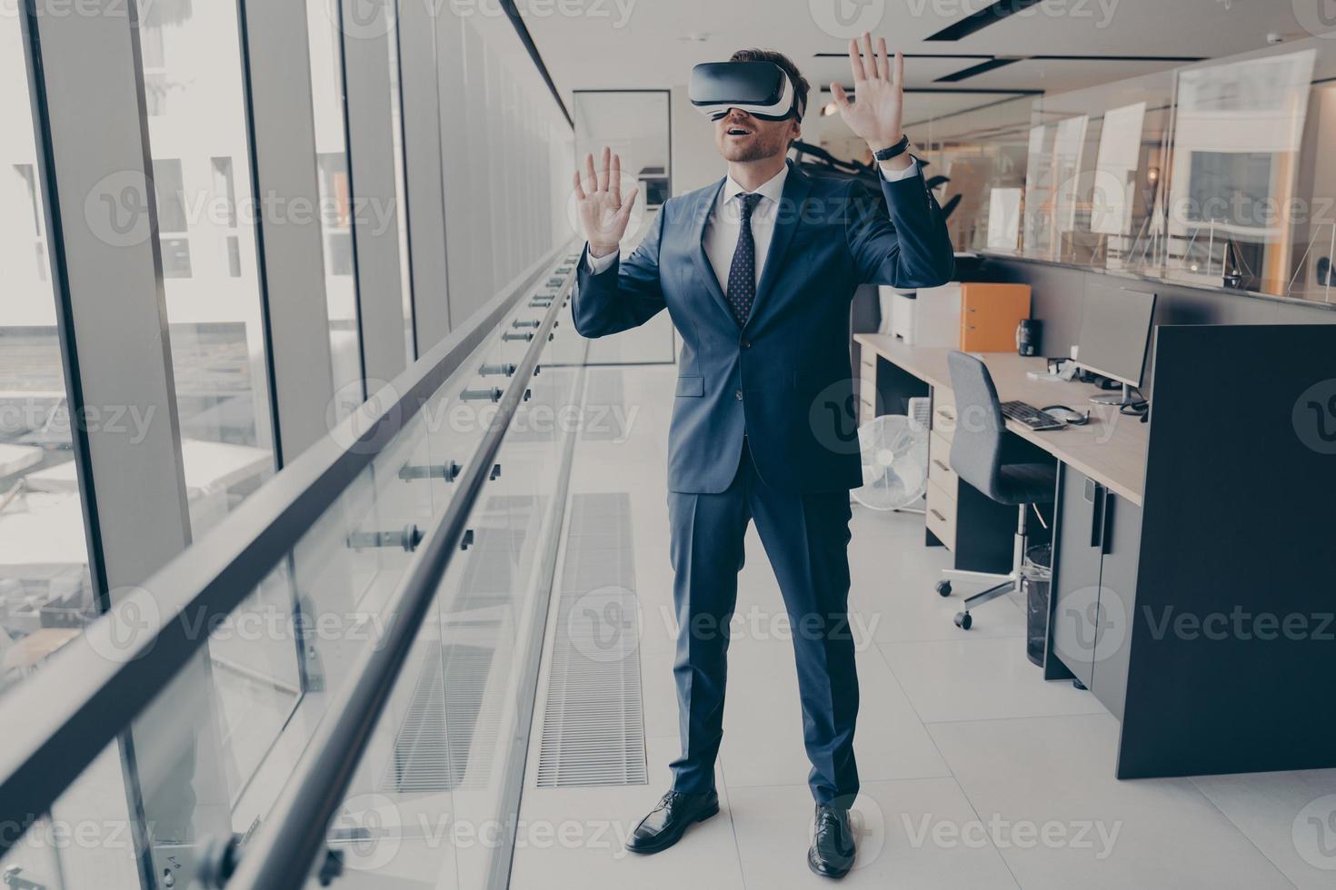 jonge verbaasde zakenman in vr-headset die iets met handen probeert aan te raken terwijl hij in een modern kantoor staat foto