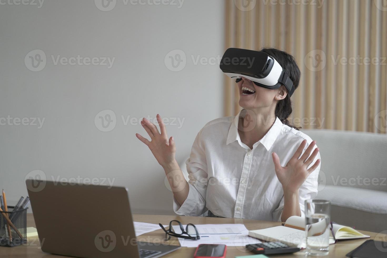 zakenvrouw draagt vr-headset voor laptop en steekt handen omhoog terwijl ze objecten in 3D-realiteit probeert aan te raken foto
