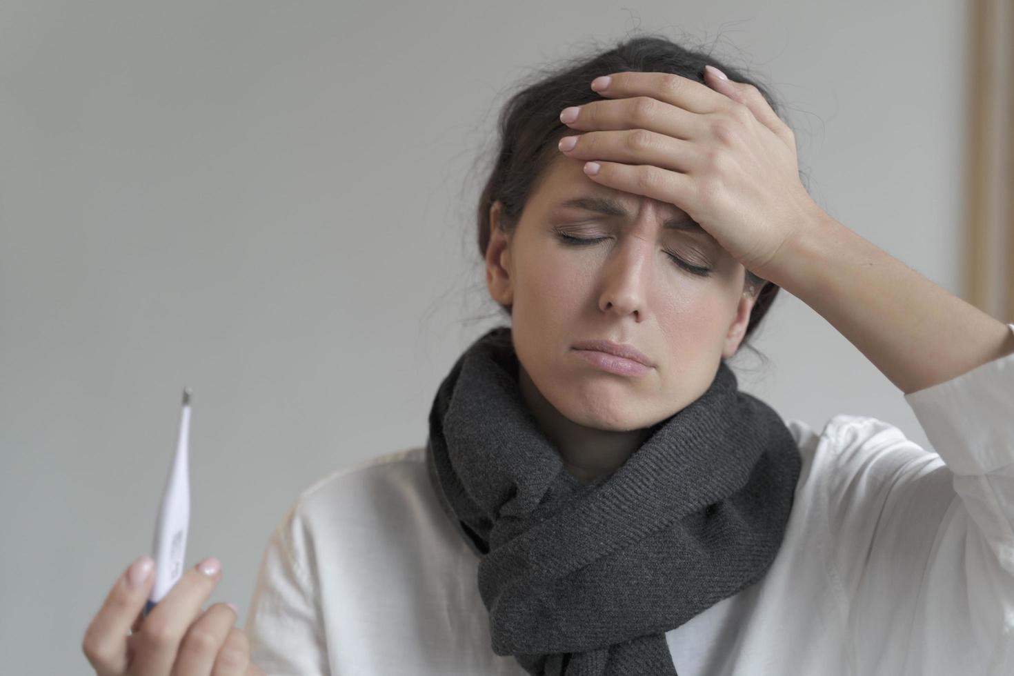 ongezonde italiaanse vrouw in warme sjaal met gesloten ogen, houdt digitale thermometer vast foto