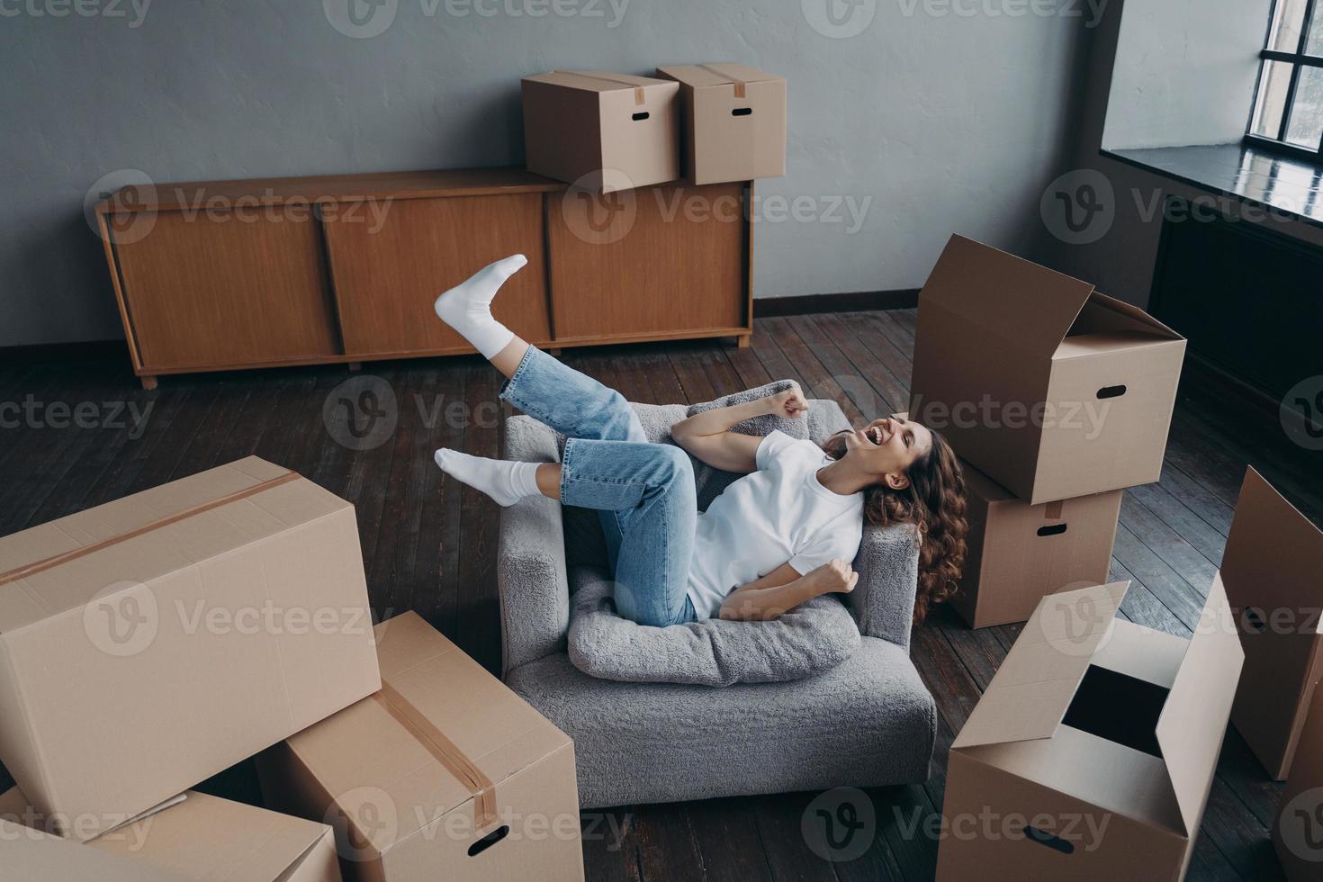 dolblij Spaanse jonge vrouw heeft een nieuw appartement gekocht. dame is ontspannen in een fauteuil. foto