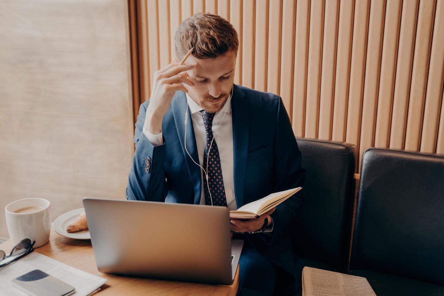 succesvolle financier in elegante smoking met doordachte blik in oordopjes en met laptop foto