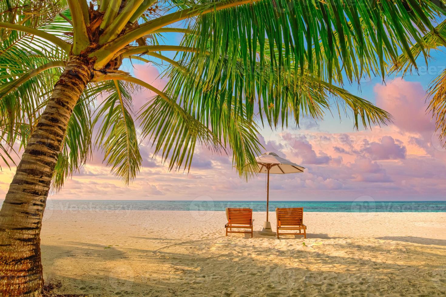 prachtig tropisch zonsonderganglandschap, twee ligbedden, ligstoelen, parasol onder palmboom. wit zand, uitzicht op zee met horizon, kleurrijke schemerhemel, rust en ontspanning. inspirerend strandresorthotel foto