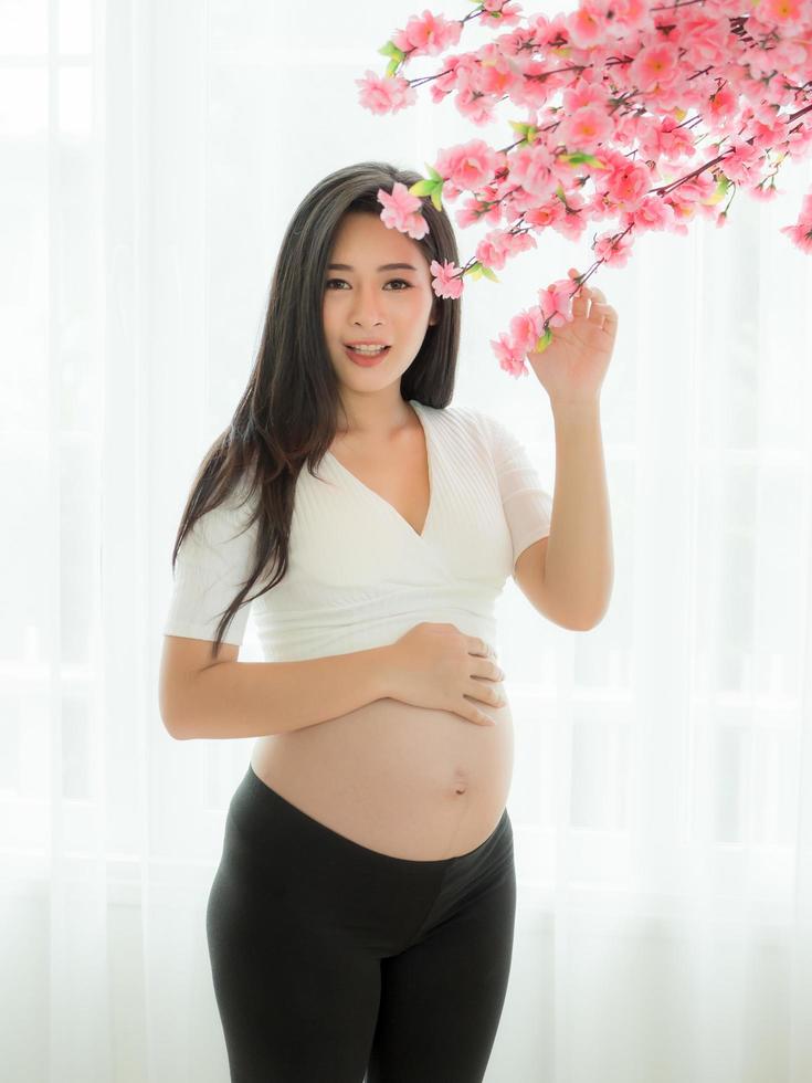 zwangere mooie vrouw staat om je buik en bloemen vast te houden in een kamer in Japanse stijl foto