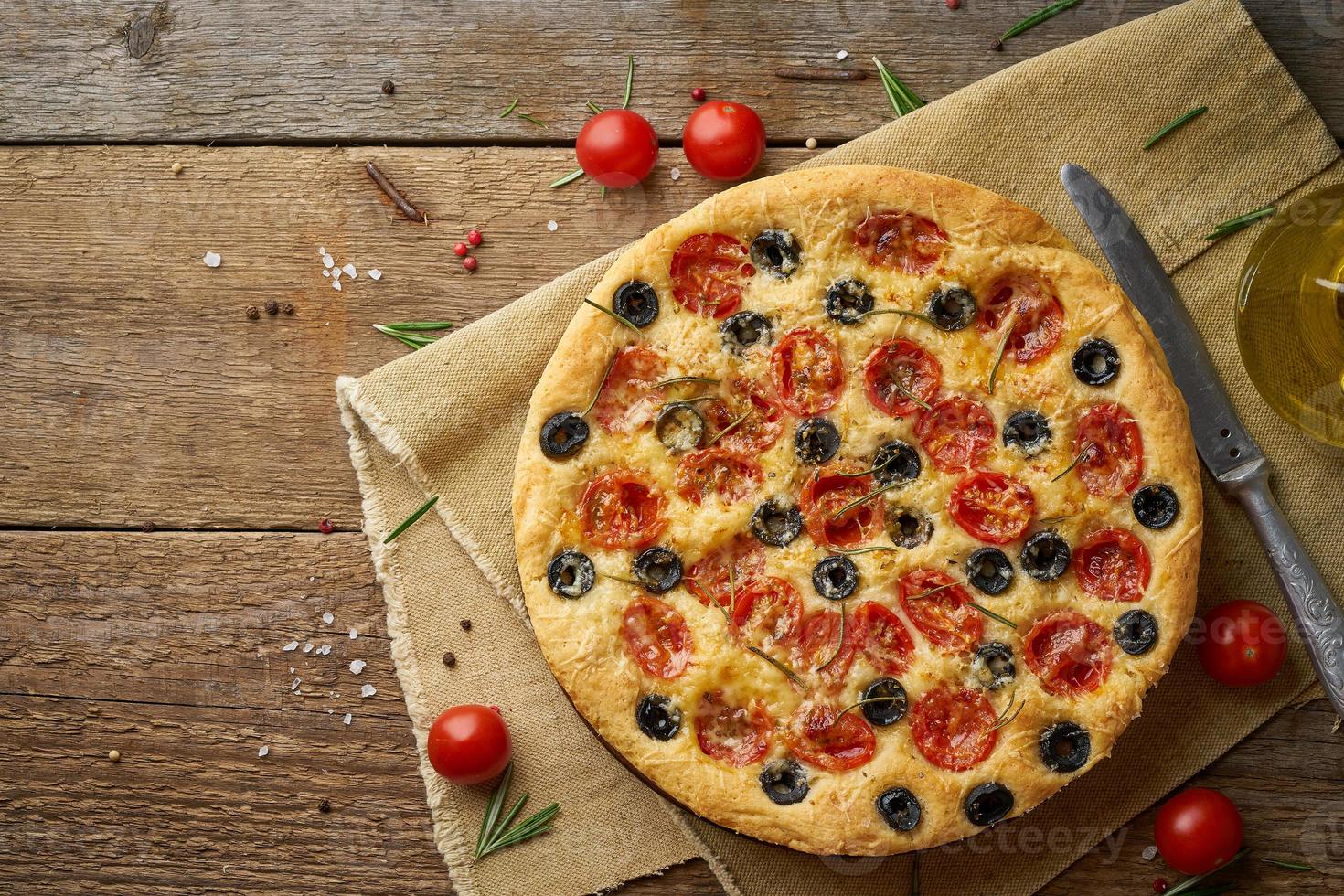 focaccia, pizza, Italiaans plat brood met tomaten, olijven en rozemarijn op houten rustieke tafel, kopieer ruimte foto