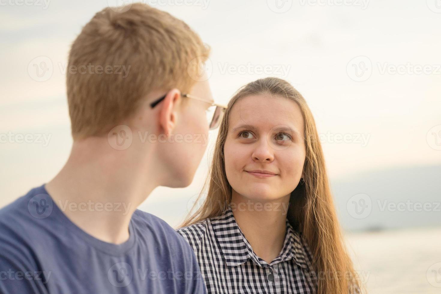 meisje kijkt naar jongen op een strand bij de zonsondergang, concept van tienerliefde foto